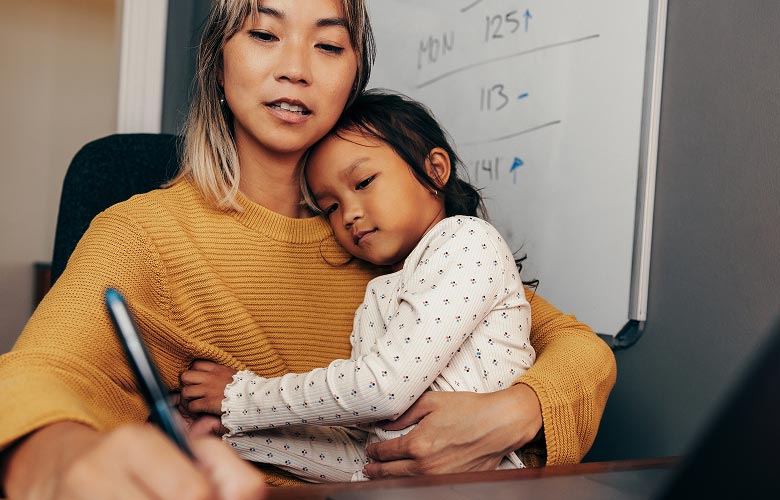 An adult who is writing something down while a child sits on their lap