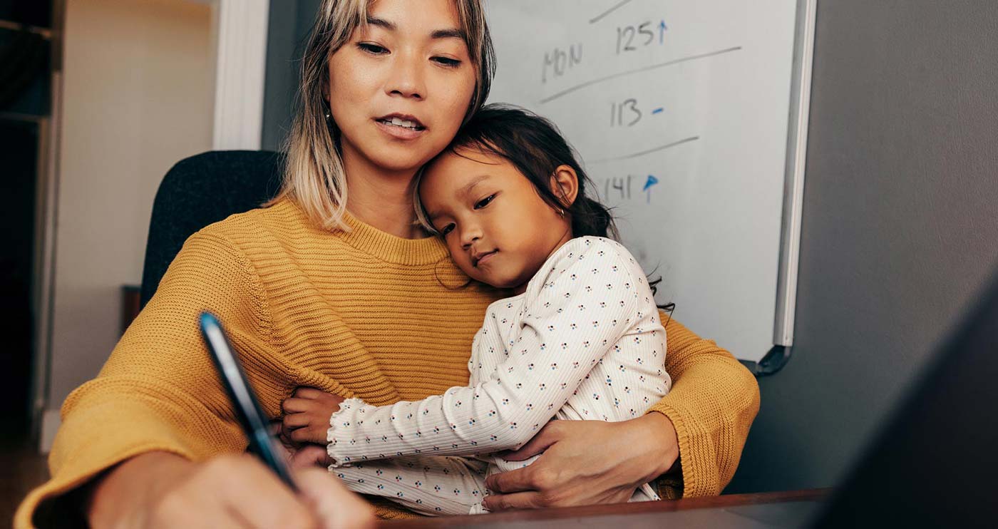 An adult who is writing something down while a child sits on their lap