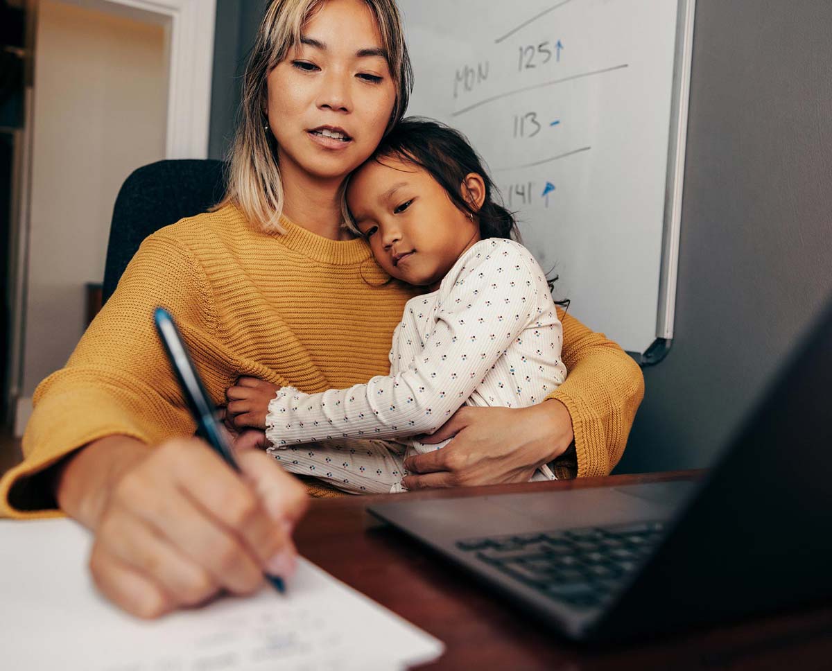 An adult who is writing something down while a child sits on their lap